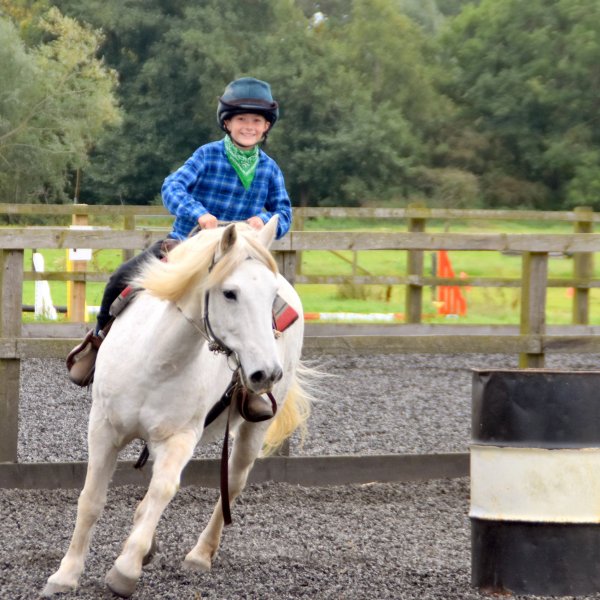 Boy smiling while riding grey horse around a black and white barrel