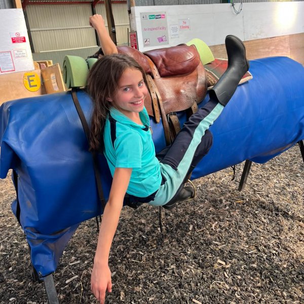 girl hanging from side of trick riding saddle
